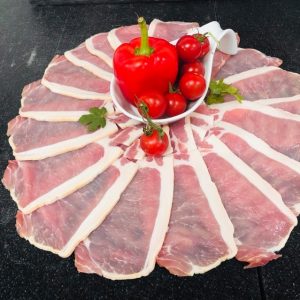 Circular arrangement of fresh unsmoked back bacon rashers with bowl at centre containing whole red pepper and cherry tomatoes