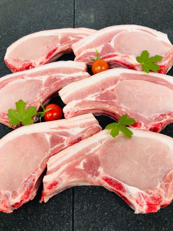 Six fresh pork chops garnished with cherry tomatoes and flat-leaf parsley