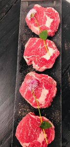 Display of four fresh ribeye steaks garnished with herbs and disted with ground salt and pepper
