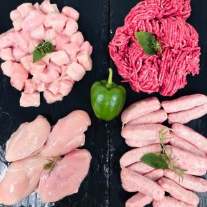 Display of fresh meats showing diced chicken, four chicken breasts, beef mince, and Cumberland sausages. Garnished with whole green pepper and fresh herbs