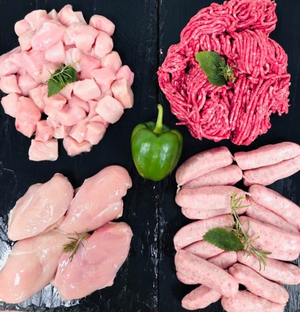 Display of fresh meats showing diced chicken, four chicken breasts, beef mince, and Cumberland sausages. Garnished with whole green pepper and fresh herbs