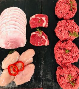 Display of fresh ribeye steaks, chicken breast fillets, beef mince and gammon ham slices, garnished with sliced red peppers and sprigs of fresh rosemary
