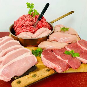Display of fresh Cumberland sausages, beef mince, sirloin steaks, pork chops, and chicken fillets, with butchers' knives and fresh herbs