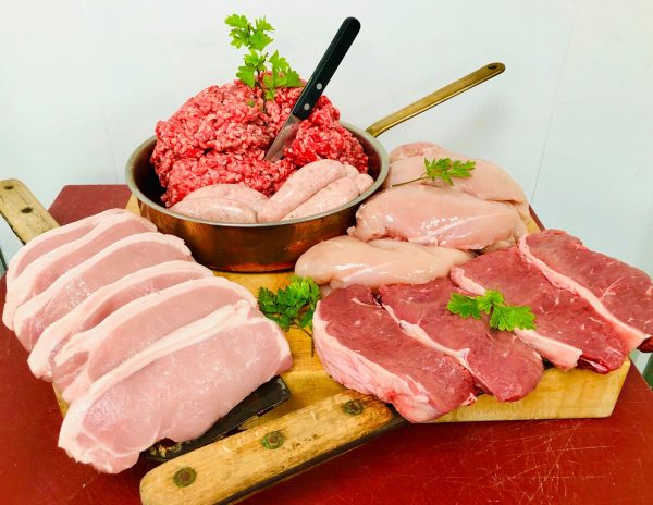 Display of fresh Cumberland sausages, beef mince, sirloin steaks, pork chops, and chicken fillets, with butchers' knives and fresh herbs
