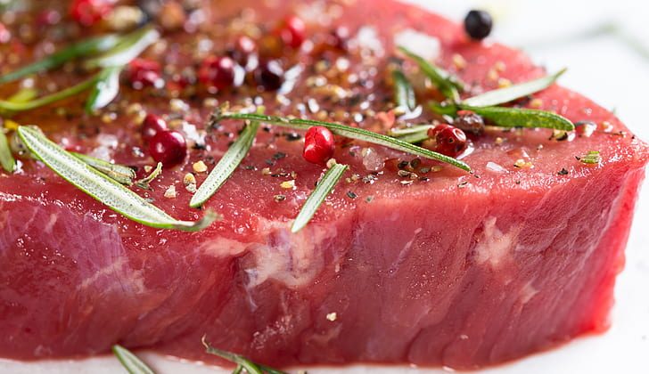 Raw steak with rosemary, salt, and peppercorns